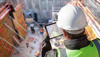一位拿着平板电脑的工程师俯视着一个多层次的商业建筑工地.